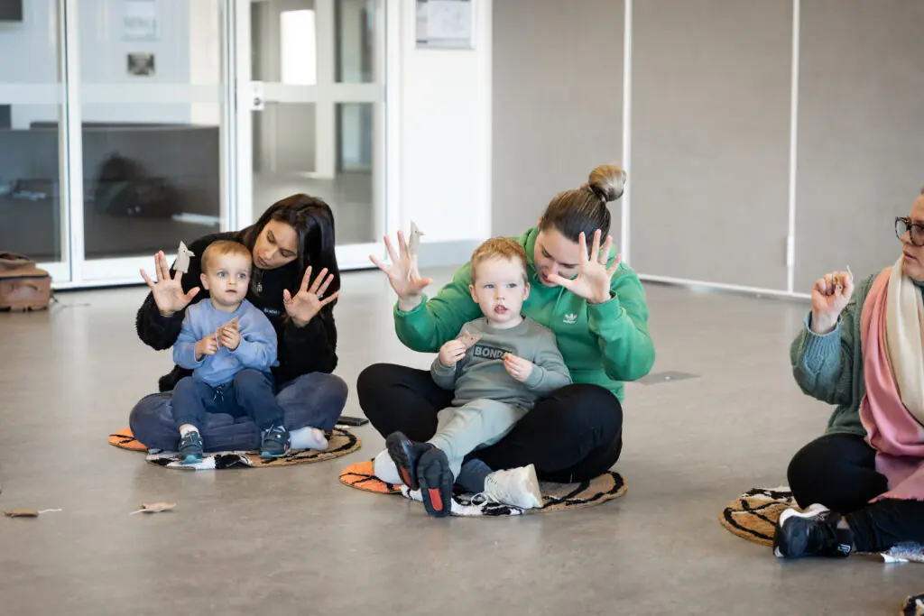 Parents and children clapping and dancing sitting on floor.